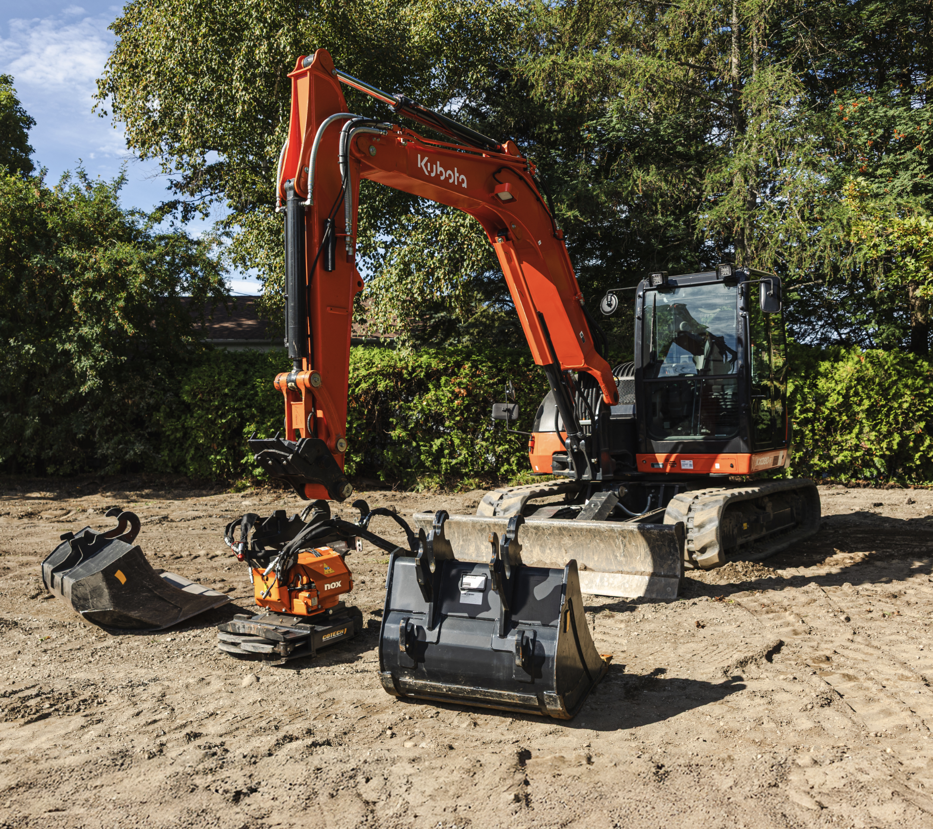 Kubota excavator with a detached orange NOX tiltrotator and two buckets arranged in front