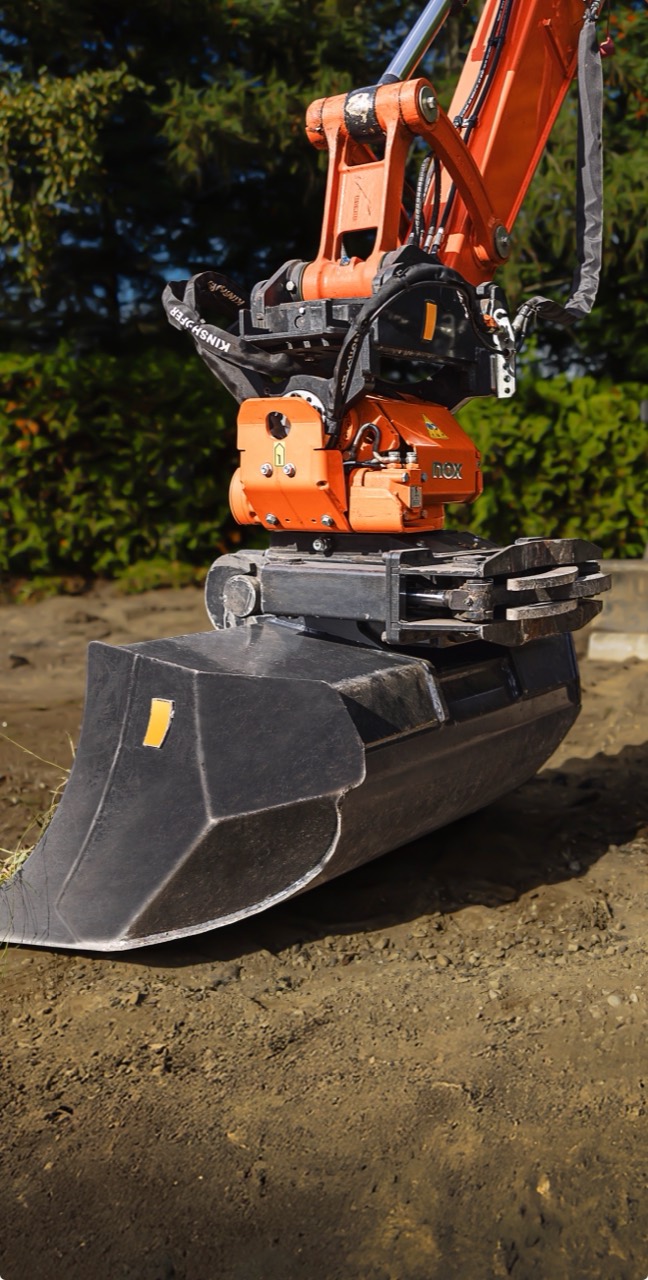Close-up of the orange NOX tiltrotator between the excavator arm and bucket