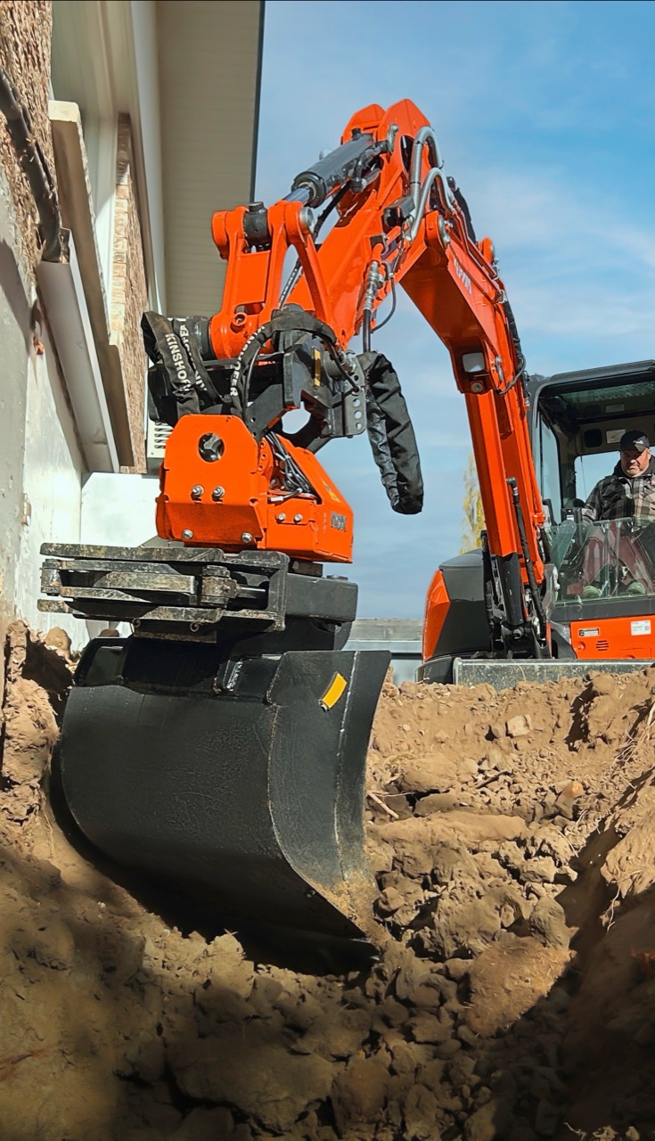 Kubota excavator with an orange NOX tiltrotator positioning its bucket beside a building